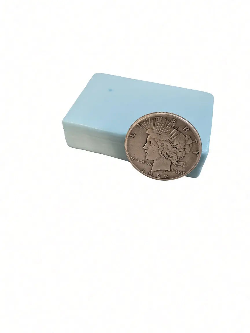Mahogany and teakwood goat milk soap bar with a genuine 1922 silver Peace dollar leaning against it, showing the coin hidden inside every bar